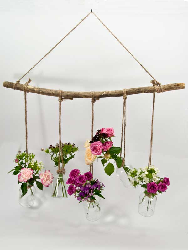 fles met bloemen hangend aan houten tak